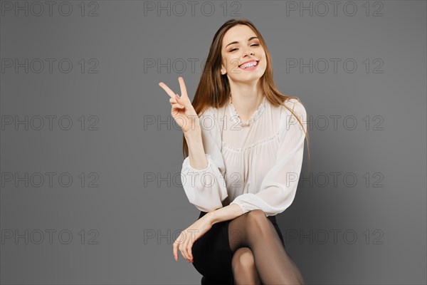 Satisfied young woman sitting on a chair raising two fingers showing a symbol of victory