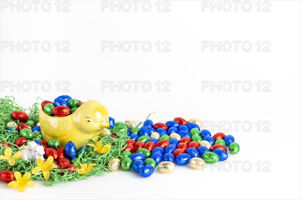 Chocolate eggs and a decorative chick surrounded by artificial grass as a festive decoration, white background