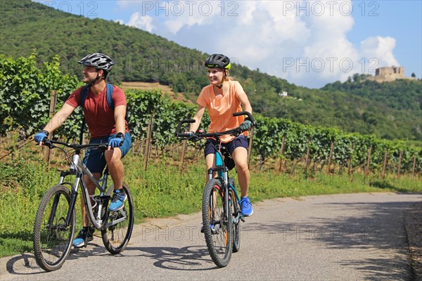 Symbolic image: Young couple on a cycle tour in the Palatinate near Maikammer. Vines and Hambach Castle in the background