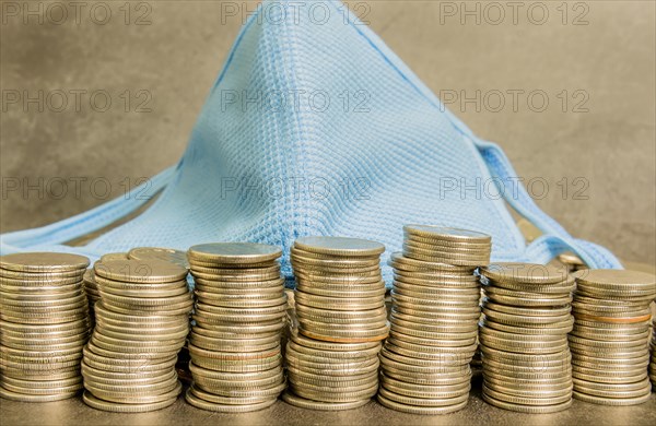 Health face mask laying on top of mound of coins on dark textured background