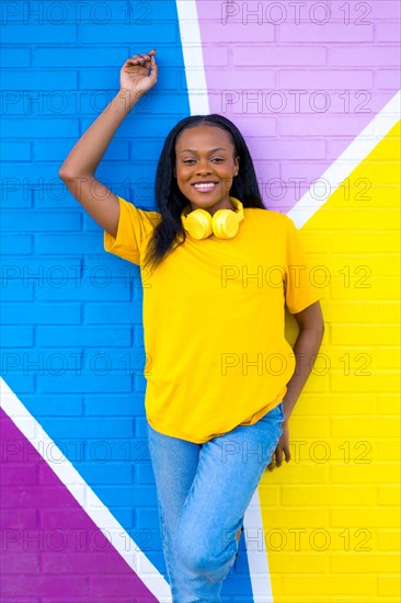 Vertical portrait of a young african woman smiling at camera next to colorful urban wall