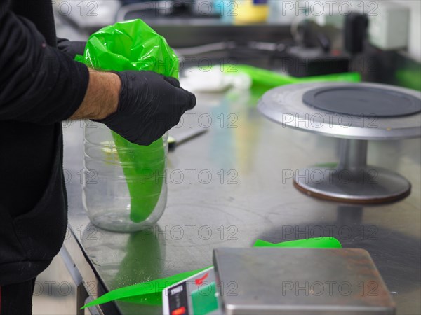 Chef's hands assembling a pastry bag with green frosting on a digital kitchen scale