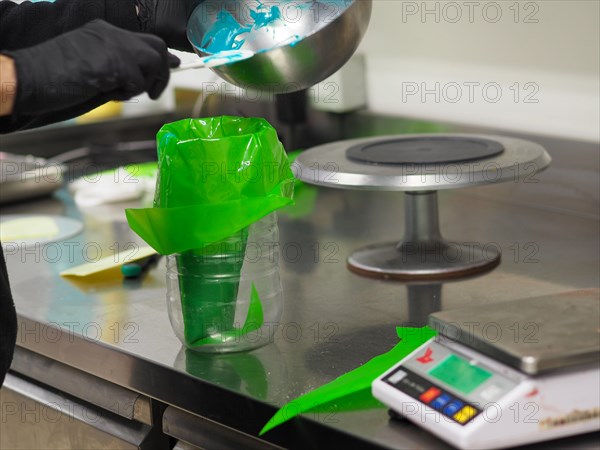 A baker skillfully filling a pastry filling bag with green icing on a kitchen scale