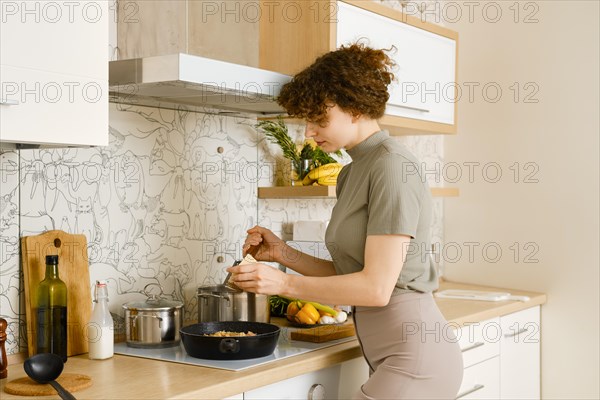 Woman grating parmesan cheese into a frying pan with cooked pappardelle pasta
