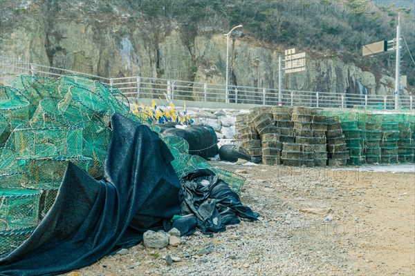 Lobster traps stacked in gravel lot with mountain cliff in background in South Korea