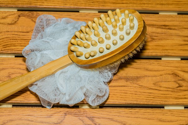 Bath and massage brush and white scrubbing pouf bath sponge on wood grain background