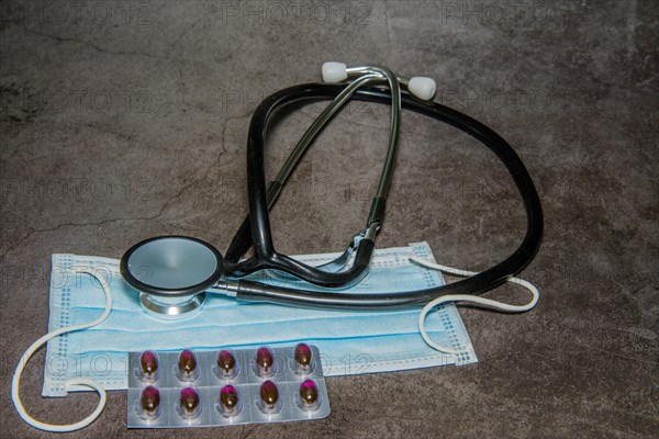 Stethoscope, disposable surgical mask and package of medicine on black background