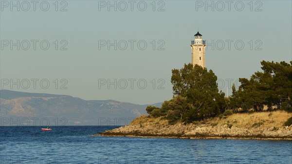 Lighthouse on a cliff surrounded by pine trees with calm sea in the evening light, Gythio, Mani, Peloponnese, Greece, Europe