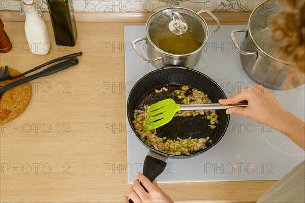 Top view of mixing chopped onion and celery into a frying pan with spatula