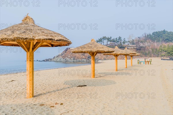Thatched covered shade pavilions on empty beach under gray winter sky