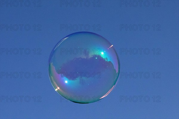 Soap bubbles coloured film of soapy water with reflection in front of blue sky