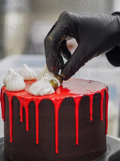 Pastry chef Gloved hand delicately placing a gold-colored chocolate sweets topping decoration on a red drip cake