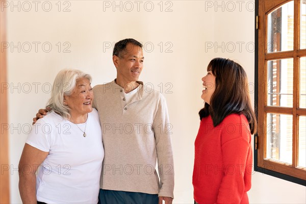 Adult children visit their Japanese-born mother, engaging in lively conversation and laughter while standing at the entrance of the home