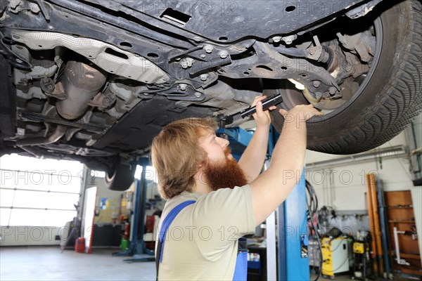 Symbolic image: Motor vehicle mechatronics technician inspects a car on the lift