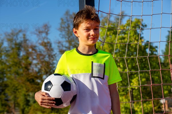 Symbolic image: Ten-year-old boy on a football pitch proudly holding a football in his arms