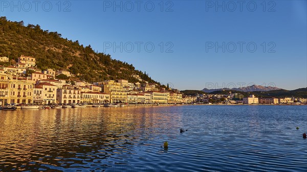 The setting sun bathes the coastal town in a warm light with reflections in the water, Taygetos Mountains, Taygetos, Gythio, Mani, Peloponnese, Greece, Europe