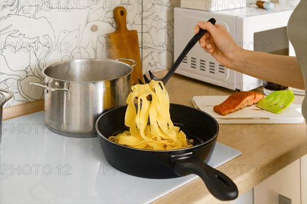 A woman transfers cooked pasta into a frying pan with fried vegetables