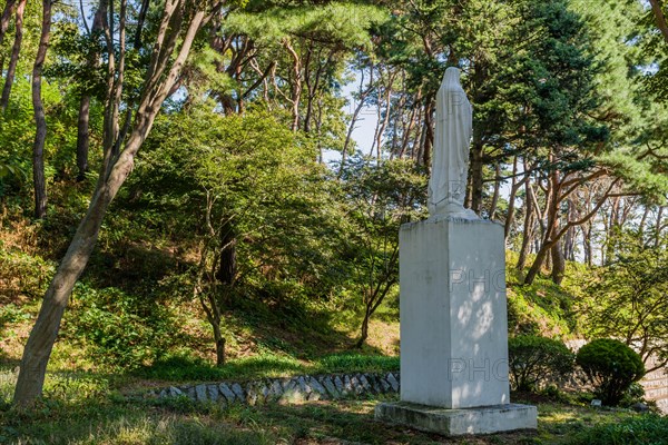 Rear view of statue of Mother Mary on plinth under shade trees at Catholic church nature park in South Korea