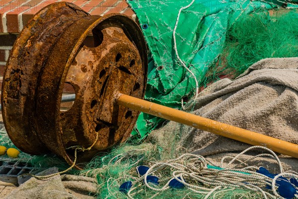 Rusted metal automobile wheel with attached yellow pole laying among fishing nets and debris in South Korea