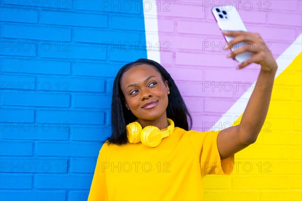 Frontal close-up portrait of an african woman smiling taking a selfie against a colorful wall