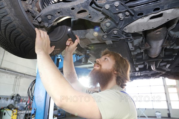 Symbolic image: Motor vehicle mechatronics technician inspects a car on the lift