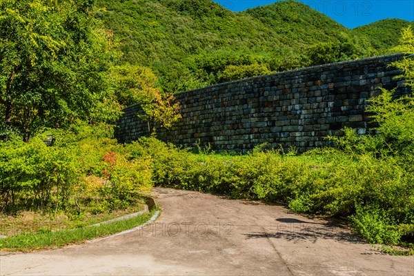 Stone block wall next to cement walking path in woodland roadside park in South Korea