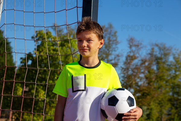 Symbolic image: Ten-year-old boy on a football pitch proudly holding a football in his arms