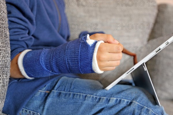 Boy with arm in plaster sits on the sofa with a tablet