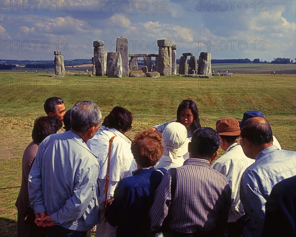 Group of Japanese tourists with guide visiting Stonehenge monument at Salisbury, England, UK, Europe. Scanned 6x6 slide