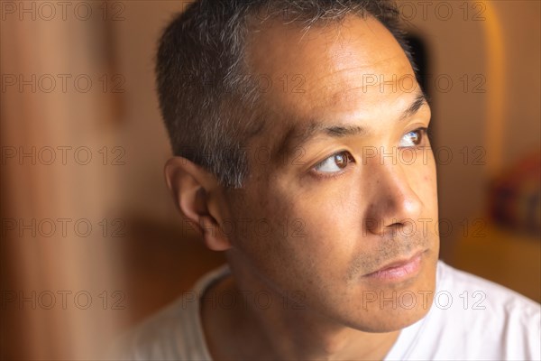 Portrait of sad Japanese young man looking at window. Close-up of an adult male of mixed latin-Japanese ethnicity gazing nostalgically out of a window