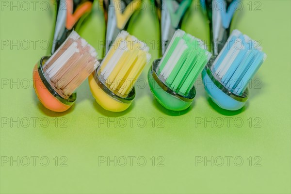 Closeup of four toothbrushes in orange, yellow, green and blue on a green background