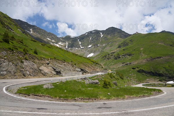 Fresh green hills and winding mountain road, partly covered by snow under a partly cloudy sky, Mountain Road, Transfogarasan High Road, Transfagarasan, TransfagaraÈ™an, FagaraÈ™ Mountains, Fagaras, Transylvania, Transylvania, Transylvania, Ardeal, Transilvania, Carpathians, Romania, Europe