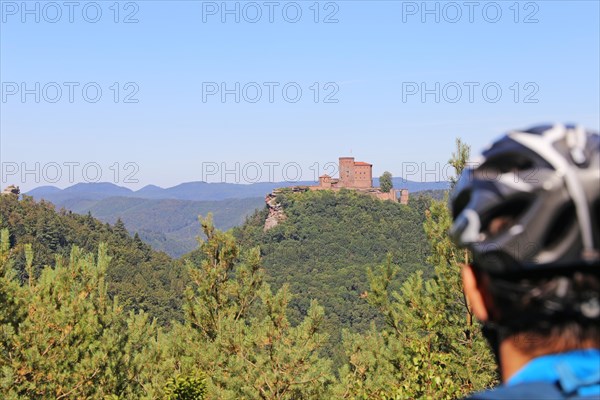 Mountain biker in the Palatinate Forest on a rock with a view of Trifels Castle, Annweiler