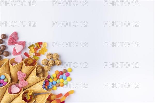 Colourful sweets, gummy bears, chocolate lentils falling out of ice cream cones, copy room, white background