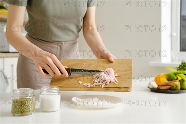 Hands of young woman dumps chopped onions onto a plate while preparing food