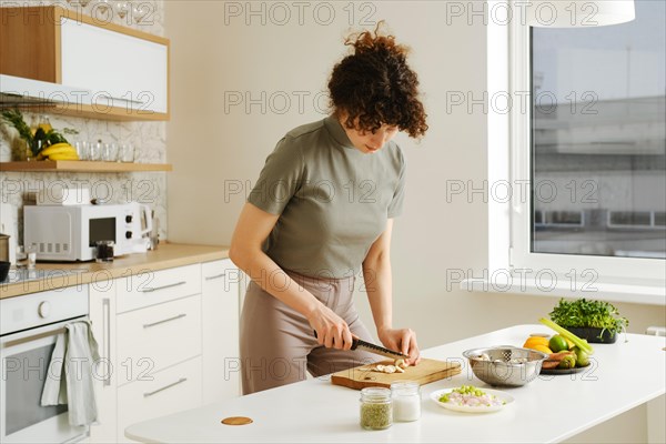 Young woman slicing fresh champignon in the kitchen on wooden cutting board