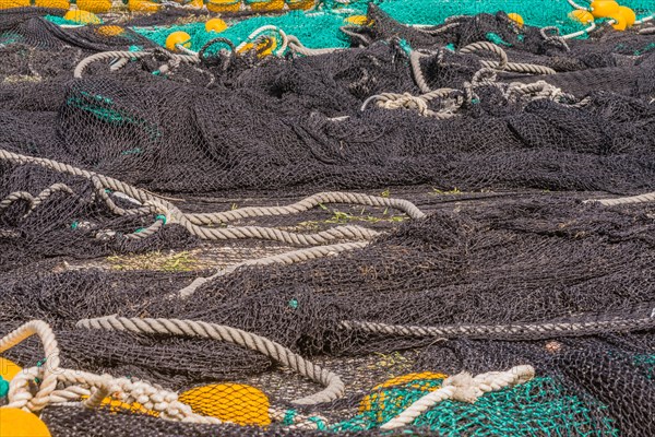 Closeup of large black and green fishing nets with yellow floats laid out on ground to dry in South Korea