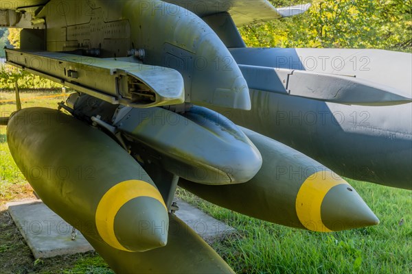 Closeup battery of bombs mounted on port side wing of jet fighter on display in public park