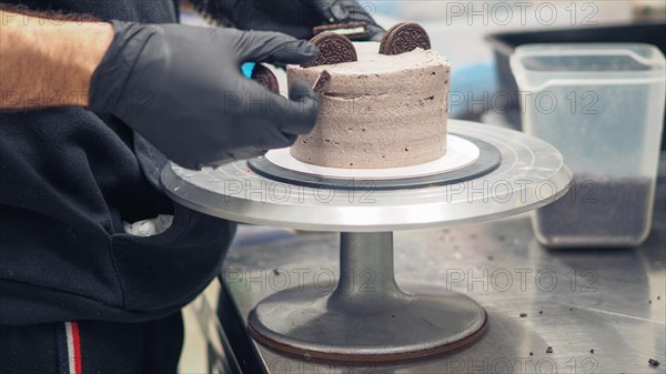Hands of a chef adding dark chocolate cookies to top a creamy chocolate frosted cake