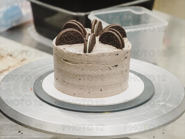 Dark chocolate cookies topping a cream cake with whole Oreos on top, on a kitchen turntable