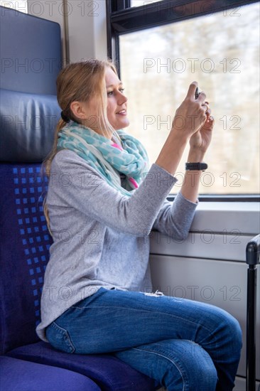 Young woman on a train takes photos of the landscape with her smartphone