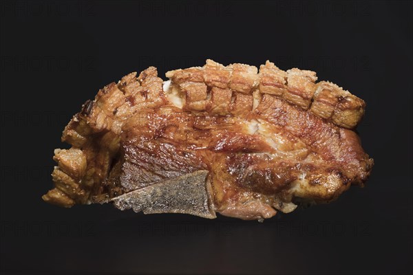 Freshly roasted pork belly with bone and crispy crust, food photography with black background