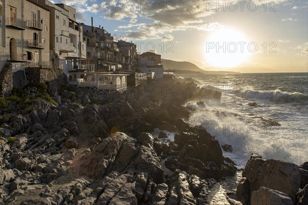 Sea water crashes against the cliffs of the rugged coastline in the town of Cefalu, Sicily, Italy, Europe