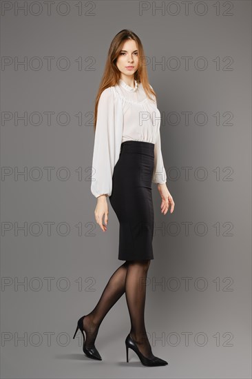 Young woman in tight pencil skirt and blouse walking on grey background
