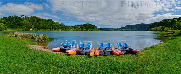 Tranquil Furnas Lake with pedal boats on the shore, surrounded by green nature and a cloudy sky, Furnas Lake, Furnas, Sao Miguel, Azores, Portugal, Europe
