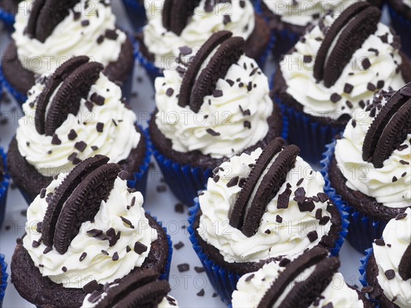 Production of A group of unhealthy dark chocolate cupcakes with sweet frosting cream and cookie toppings in blue liners