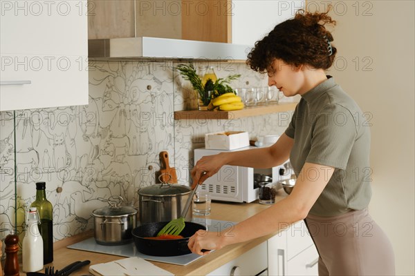 Woman flipping trout in a frying pan while preparing dinner in her kitchen