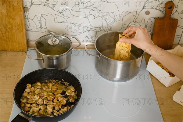 View from above at female hand adding pappardelle pasta into pot with boiling water