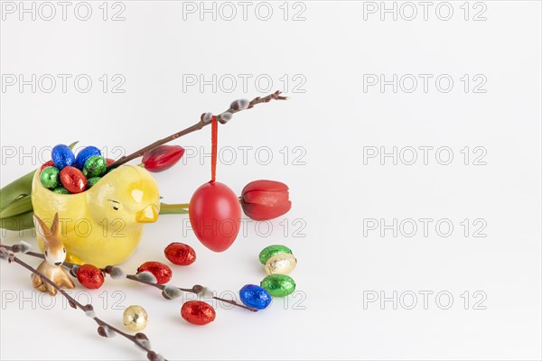 Red Easter egg hanging on a willow branch with tulips and chocolate eggs, white background, copy space