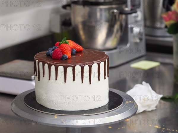 A finished chocolate drip cake topped with an assortment of fresh berries